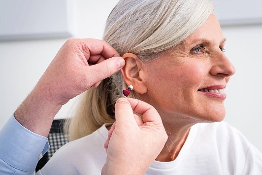 Ältere Frau bekommt ein modernes Hörgerät eingesetzt und lächelt zufrieden im Profil.